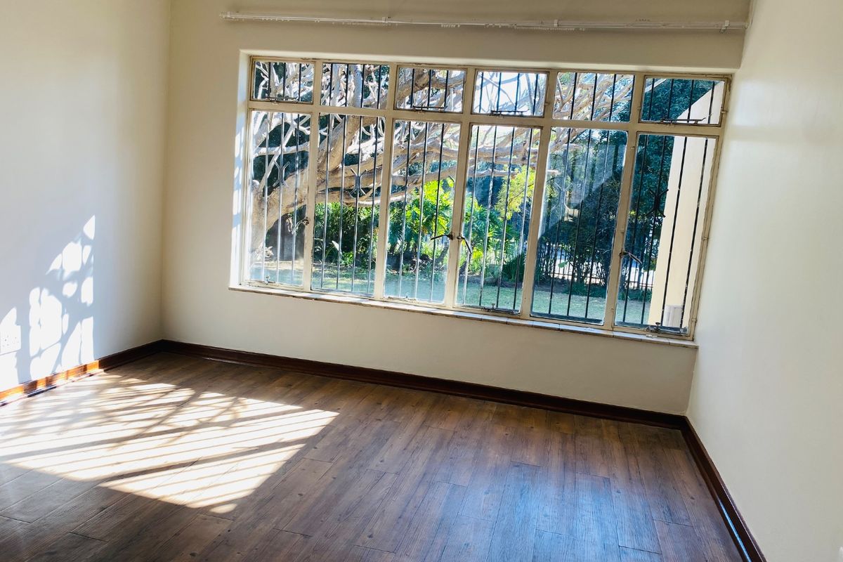 A bright, empty bedroom featuring laminate flooring, large windows with security bars, and neutral walls, offering a clean canvas for personalization.