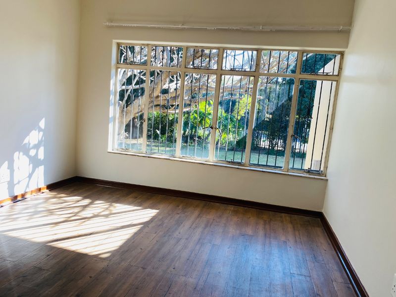 A bright, empty bedroom featuring laminate flooring, large windows with security bars, and neutral walls, offering a clean canvas for personalization.