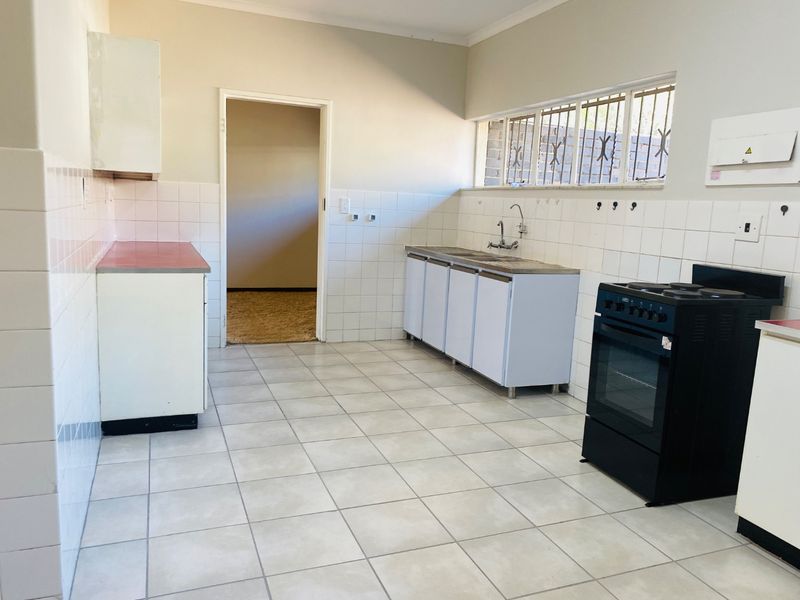 A functional, empty kitchen featuring tiled flooring, a stainless steel sink, and a freestanding electric stove, ready for modernization and personal touches.