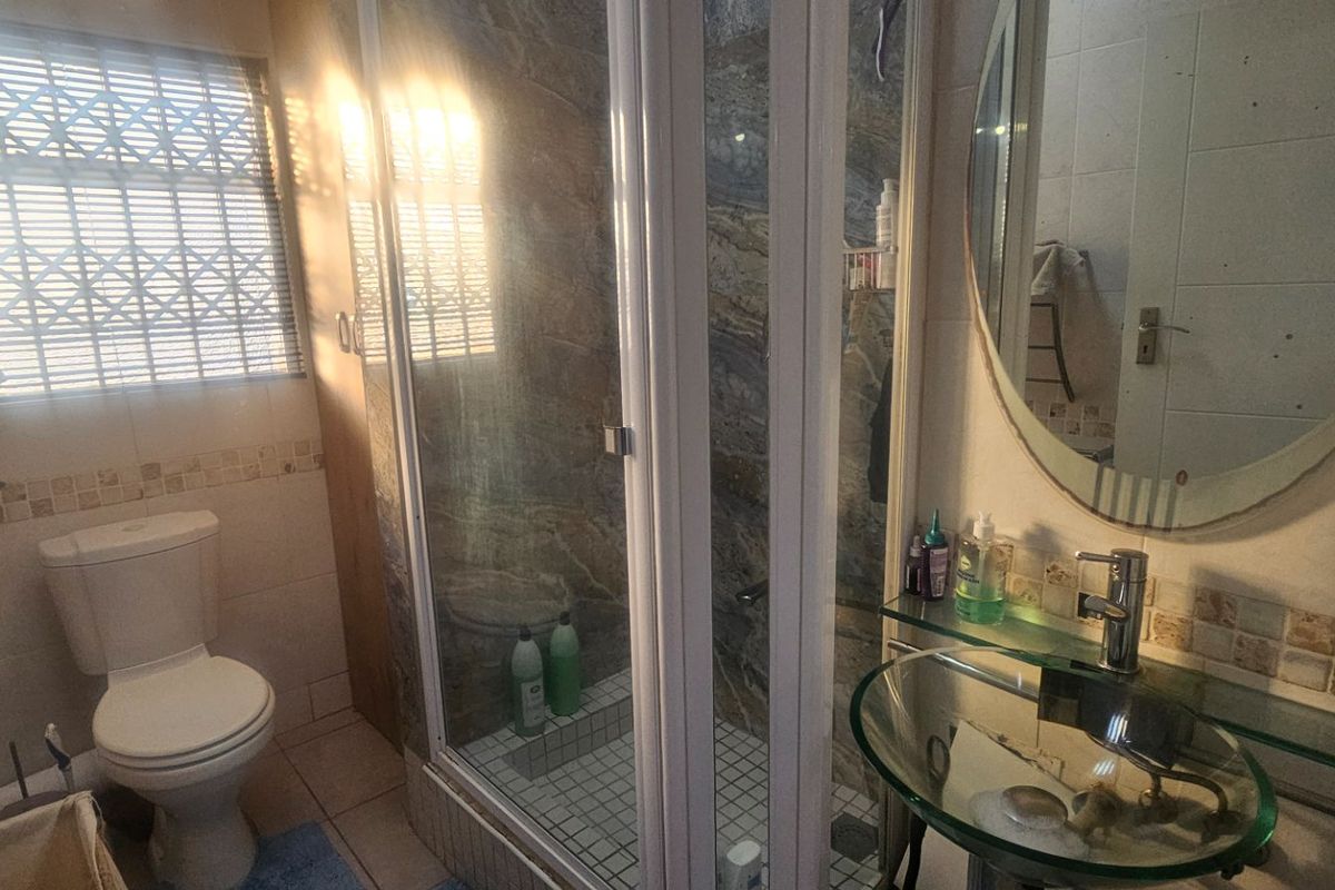 A functional bathroom featuring a glass vessel sink, a shower enclosure with tiled walls, and a standard toilet, with natural light from the window.