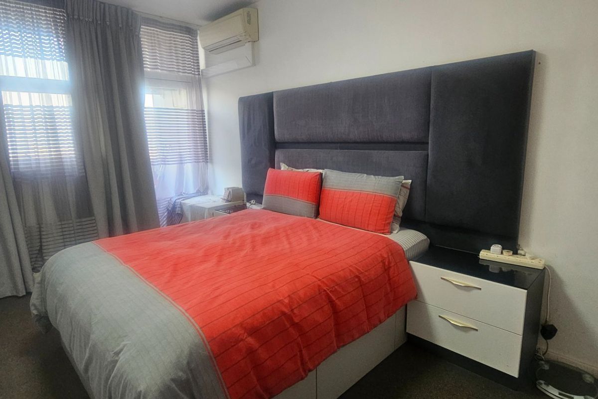 A well-maintained bedroom featuring a large upholstered headboard, split-system air conditioning unit, and floor-to-ceiling curtain treatments.