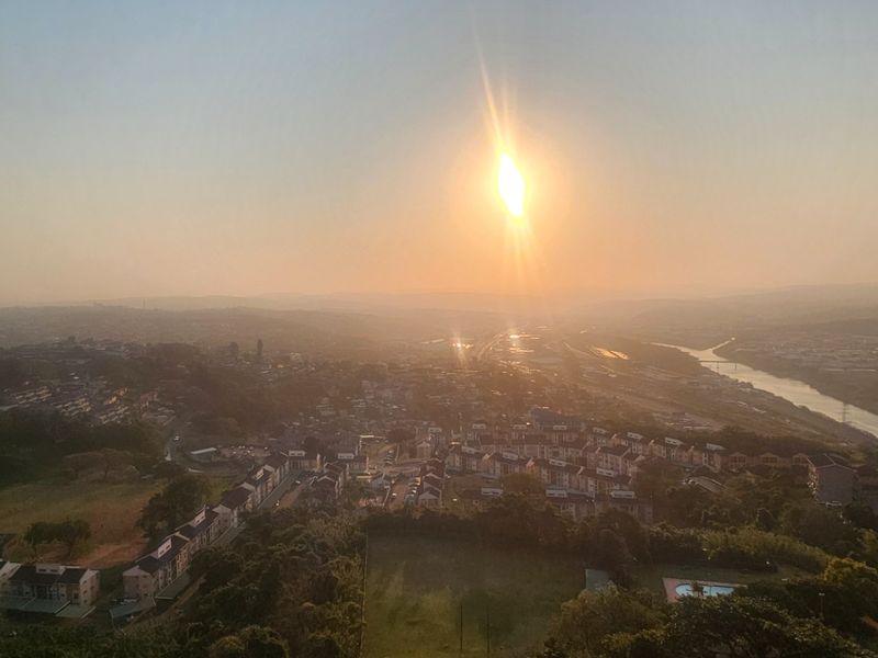 An elevated panoramic view overlooking the surrounding residential landscape, river, and horizon during sunset.