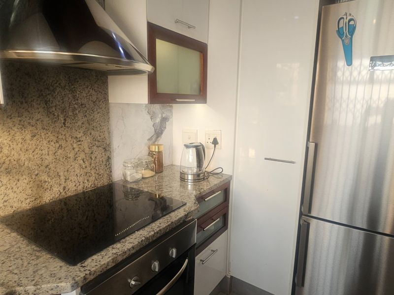 A compact kitchen featuring granite countertops, built-in cabinetry, an electric hob with extractor fan, and a built-in oven.