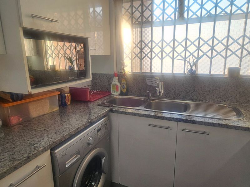 A functional kitchen featuring granite countertops, high-gloss cabinetry, a stainless steel double sink, and a built-in microwave with security bars on the window.