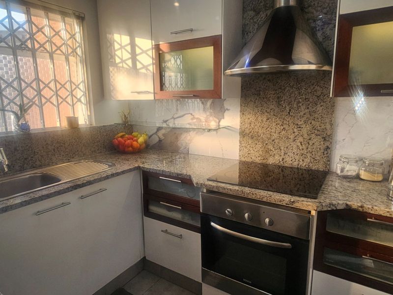 A functional kitchen featuring granite countertops, built-in oven, electric hob, extractor fan, and ample cabinetry, complemented by a window with a security gate.