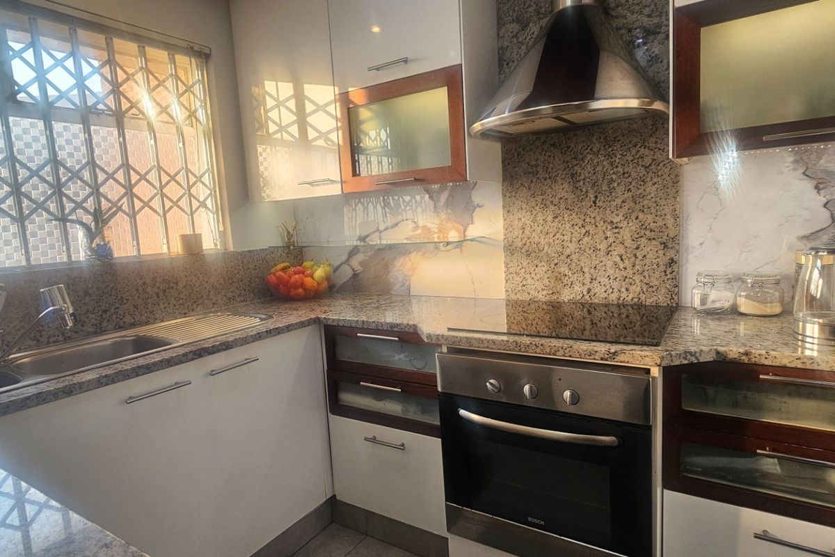 A functional kitchen featuring granite countertops, built-in cabinetry, a stainless steel oven, hob, and extractor fan, with a security gate on the window.