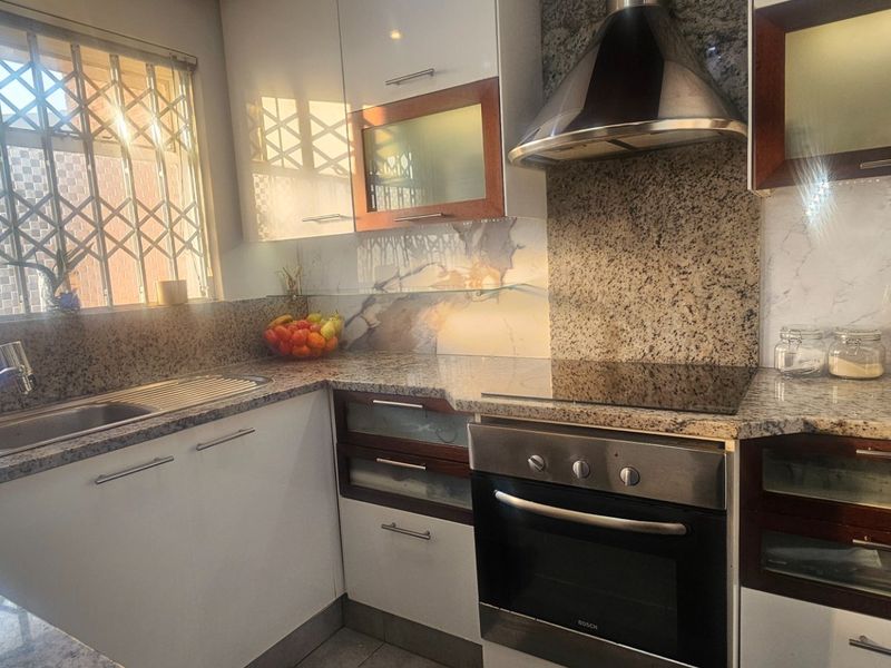 A functional kitchen featuring granite countertops, built-in cabinetry, a stainless steel oven, hob, and extractor fan, with a security gate on the window.