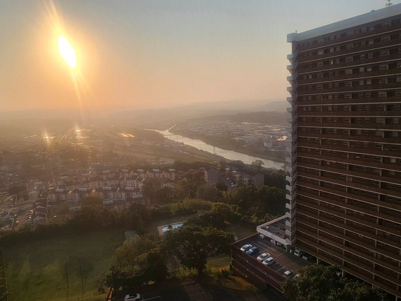Elevated panoramic view overlooking the surrounding urban landscape, river, and neighboring high-rise residential buildings at sunset.