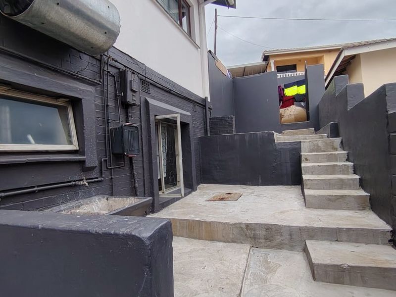 Rear exterior area featuring concrete stairs, a paved patio, retaining walls, and a mounted solar geyser unit on the building facade.