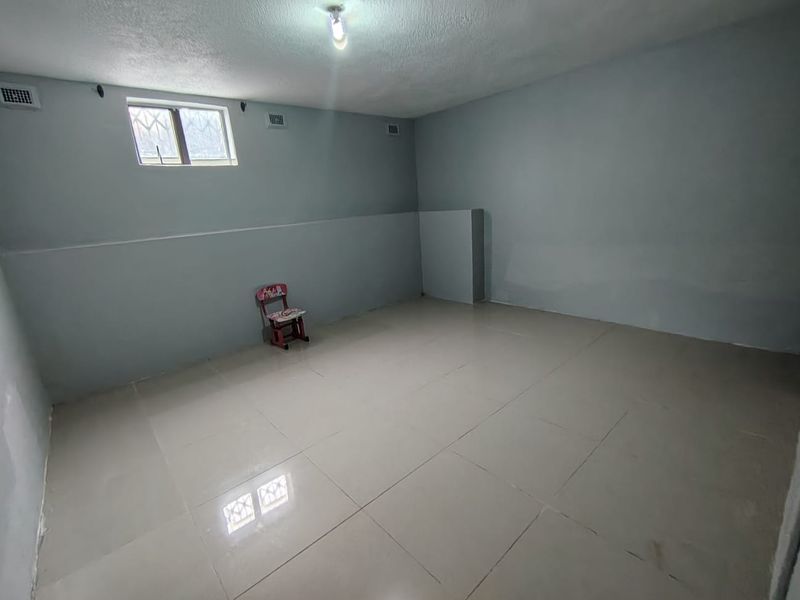 An empty, neutrally painted room featuring tiled flooring, security bars on the window, and basic ventilation grilles, offering a blank canvas for renovation.
