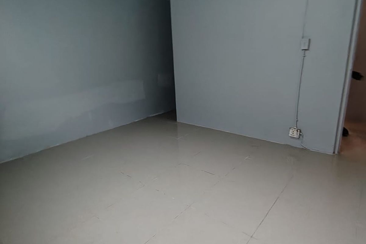 An empty, neutral-toned living area featuring tiled flooring and visible surface-mounted electrical wiring, offering a blank canvas for renovation or interior design.