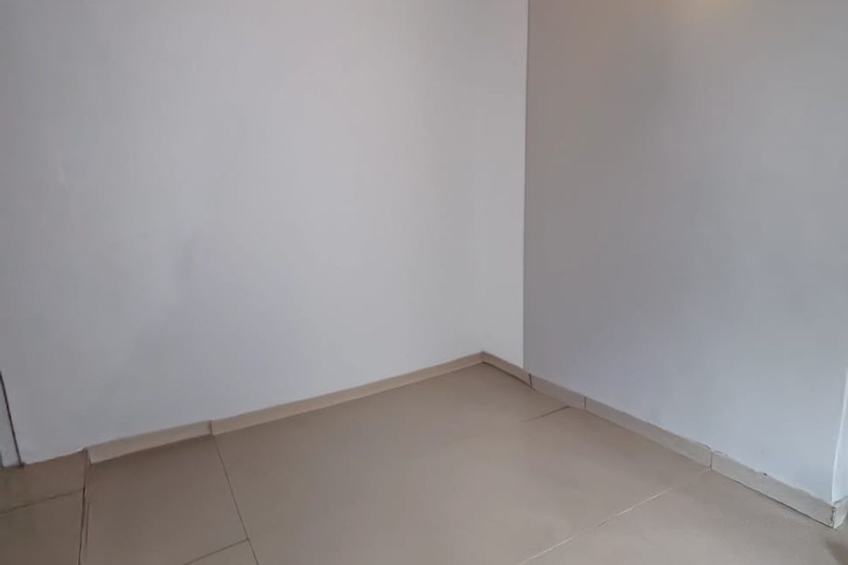 An empty, neutral-toned room featuring tiled flooring and a wall-mounted light fixture, offering a blank canvas for personalization.