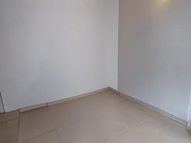 An empty, neutral-toned room featuring tiled flooring and a wall-mounted light fixture, offering a blank canvas for personalization.