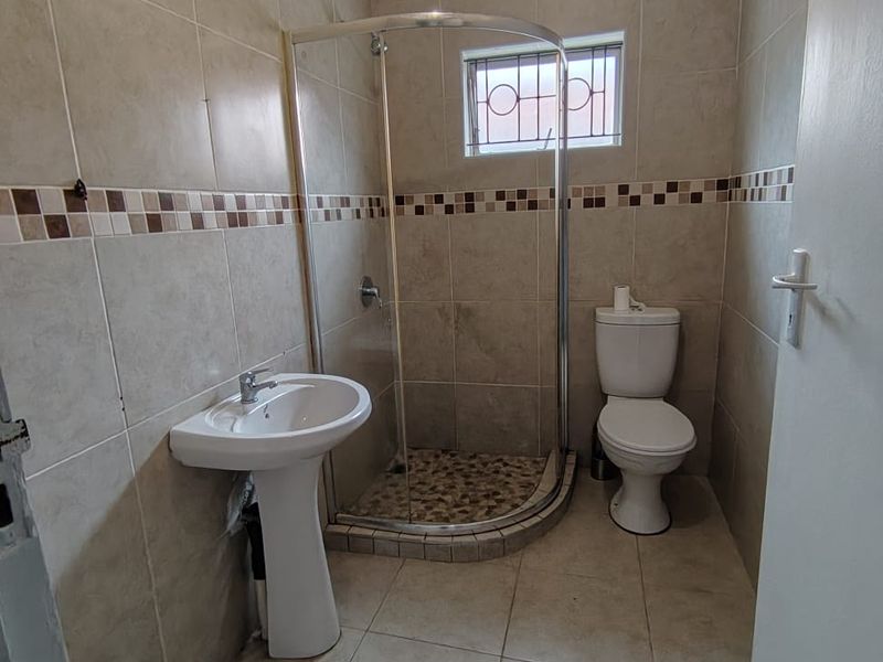 A functional bathroom featuring a corner shower enclosure, pedestal washbasin, and toilet with neutral wall and floor tiling.