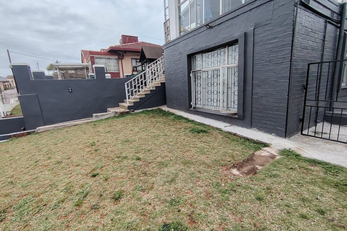 Rear exterior view of the property featuring a painted brick facade, external staircase with metal balustrade, and a small lawn area.