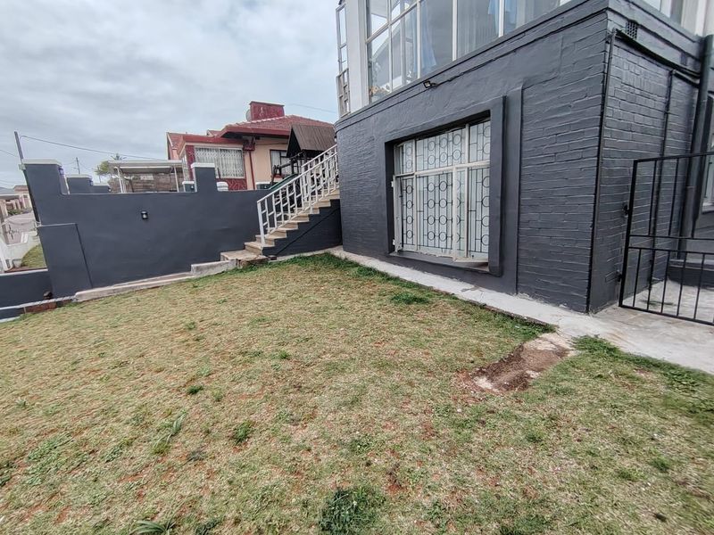 Rear exterior view of the property featuring a painted brick facade, external staircase with metal balustrade, and a small lawn area.