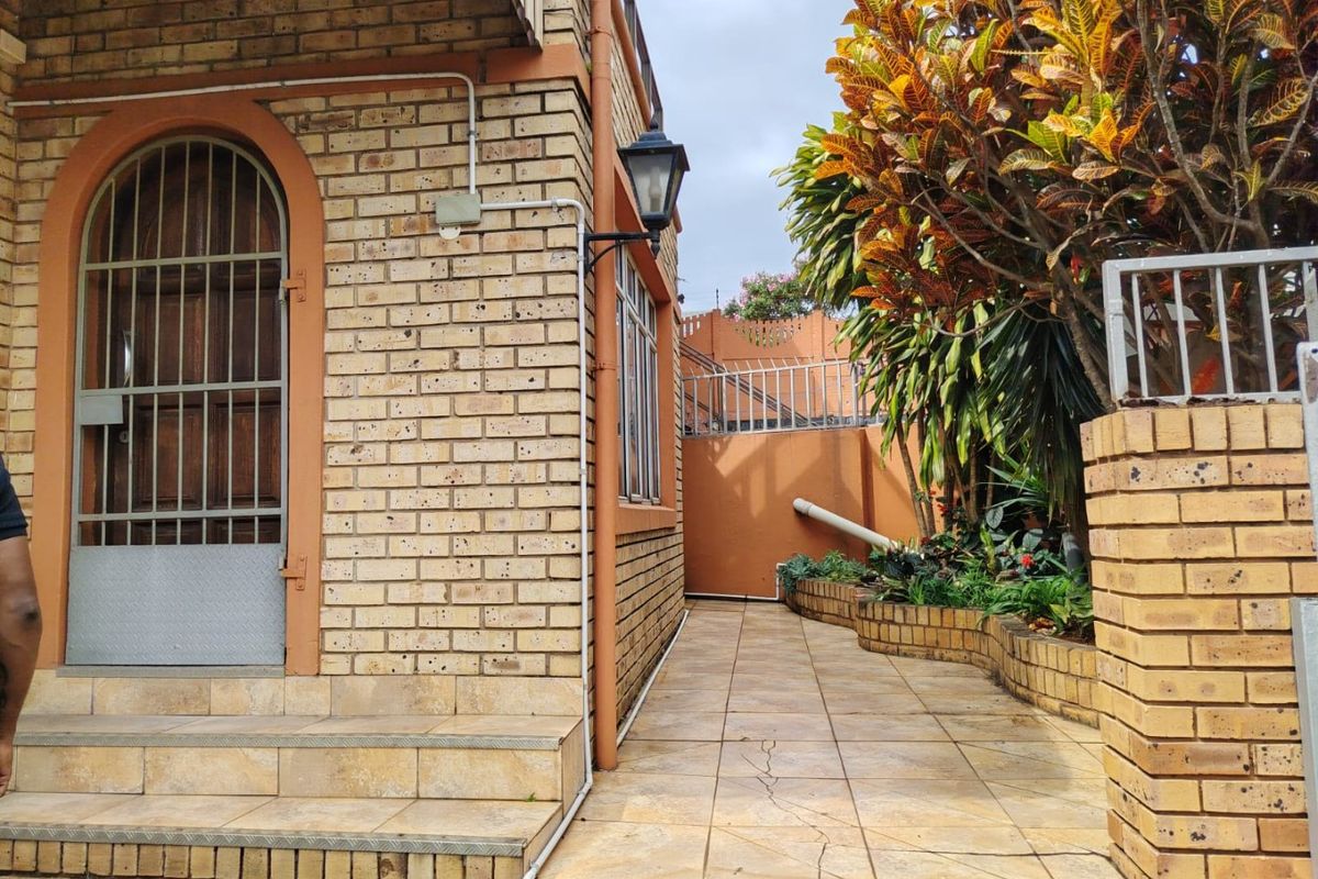 A side exterior view of the property featuring face brick walls, a tiled walkway, and a secure entrance with a metal gate.