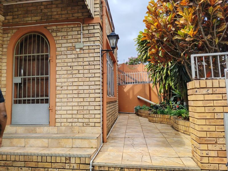 A side exterior view of the property featuring face brick walls, a tiled walkway, and a secure entrance with a metal gate.