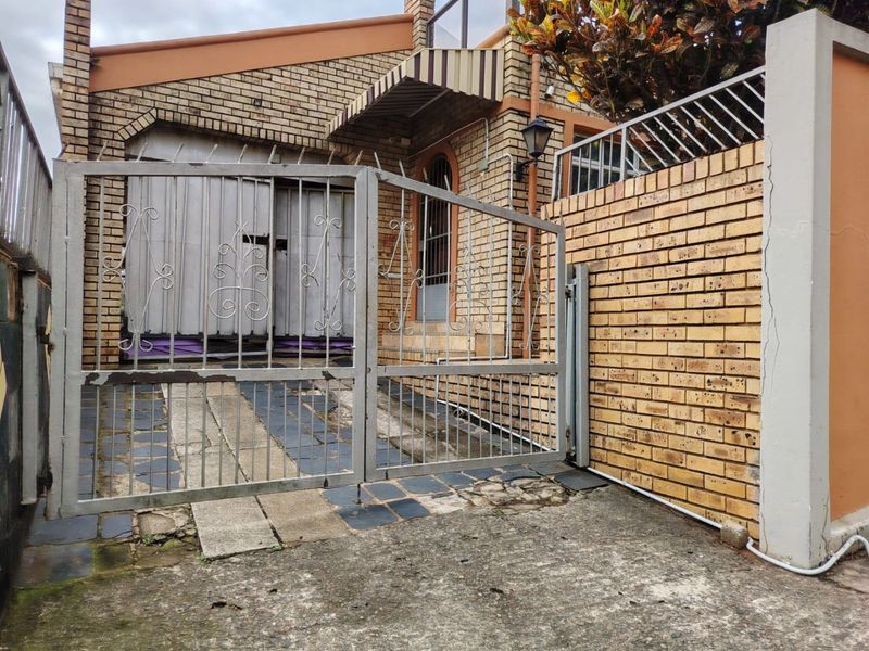 Front exterior view of a face brick house featuring a metal security gate, paved driveway, and a brick boundary wall.