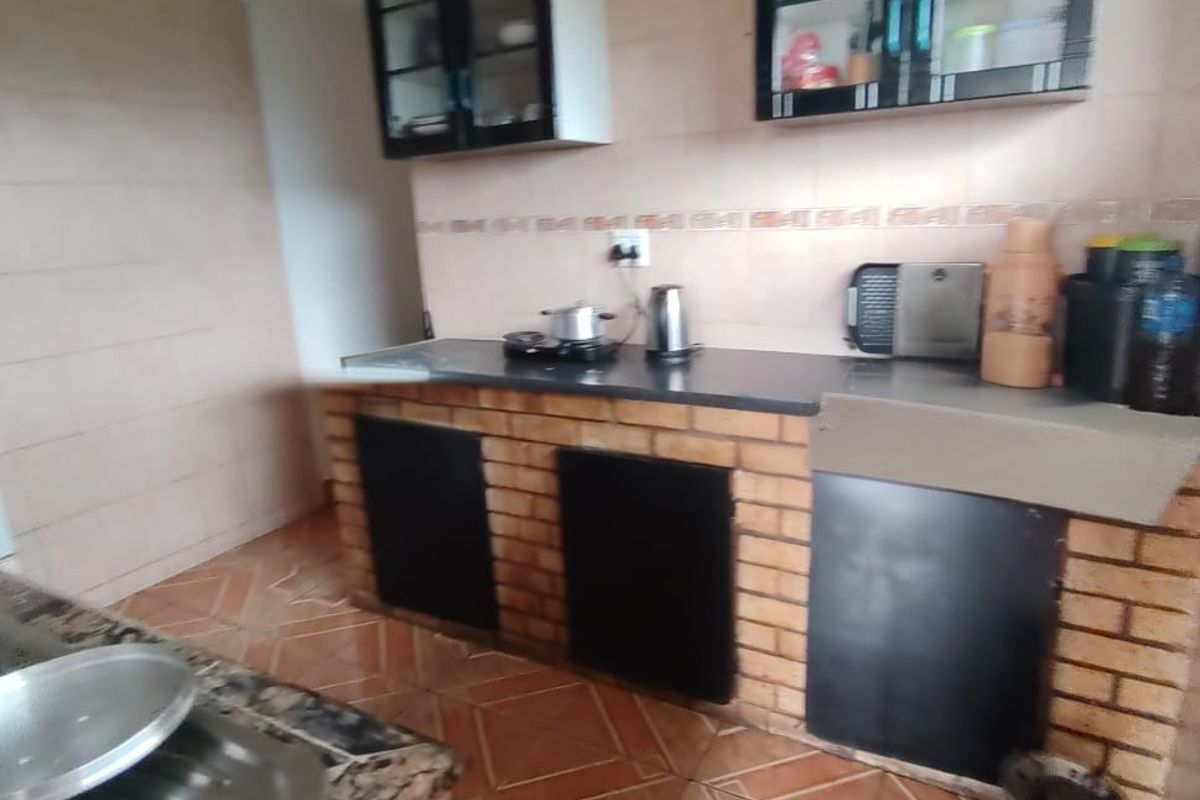 A functional kitchen featuring brick-based cabinetry, granite countertops, tiled backsplash, and upper glass-front storage cabinets with tiled flooring throughout.
