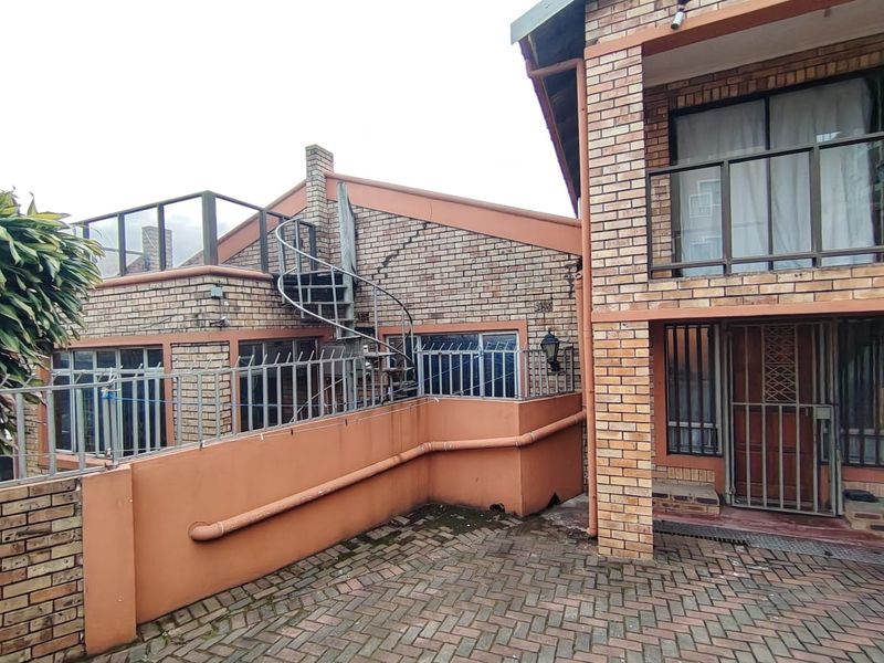 Rear exterior view of a face brick house featuring a spiral staircase, paved courtyard, and balcony, showing visible structural cracking in the brickwork.