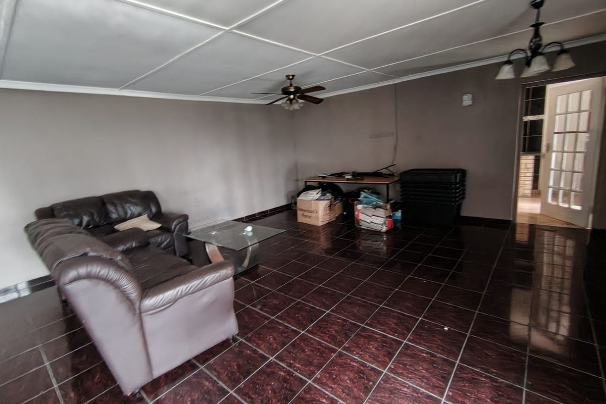 A living room featuring dark tiled flooring, a ceiling fan, and a panelled ceiling, offering a blank canvas for potential interior updates.