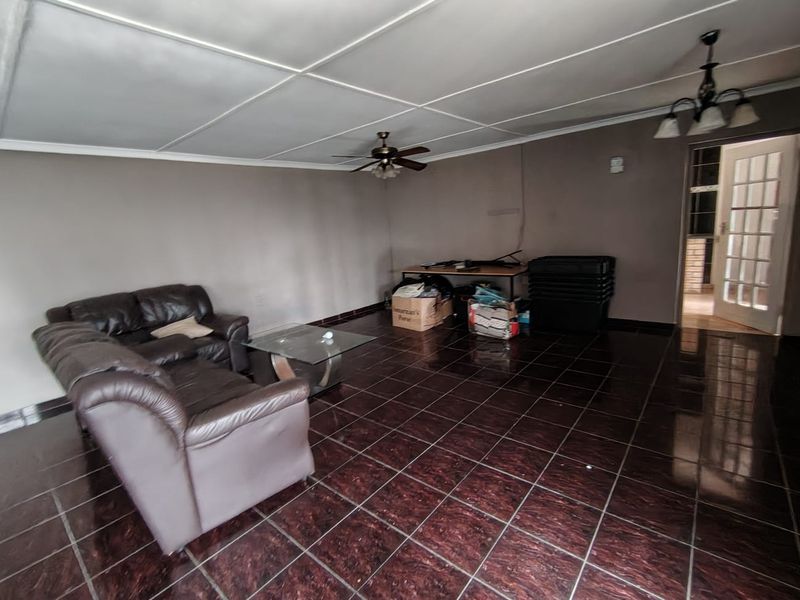 A living room featuring dark tiled flooring, a ceiling fan, and a panelled ceiling, offering a blank canvas for potential interior updates.