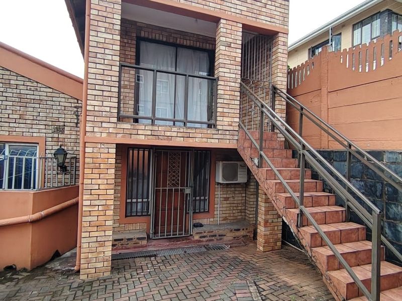 Two-story face brick exterior featuring a paved courtyard, external tiled staircase with metal railings, and an upper-level balcony.