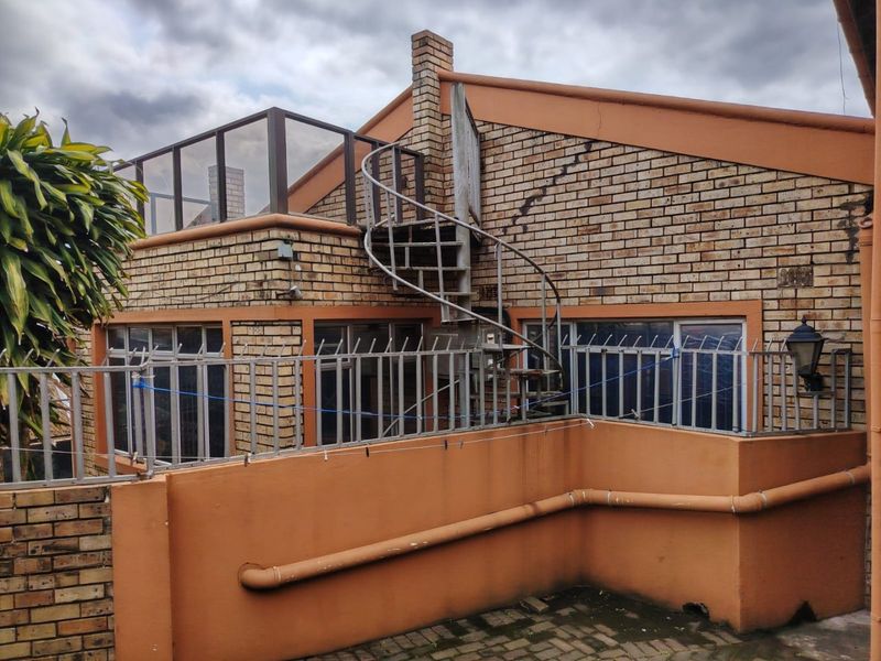 Rear exterior view featuring a brick facade, a metal spiral staircase leading to an upper balcony, and perimeter security fencing.