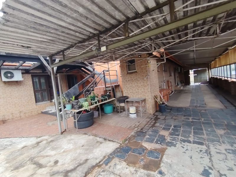 A large covered outdoor patio area featuring a corrugated metal roof, concrete and stone paving, and an external staircase leading to the upper level.