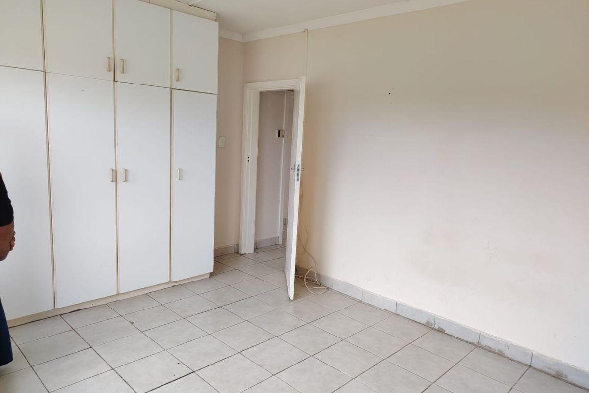 A vacant bedroom featuring white built-in cupboards and neutral tiled flooring, offering a blank canvas for potential interior updates.