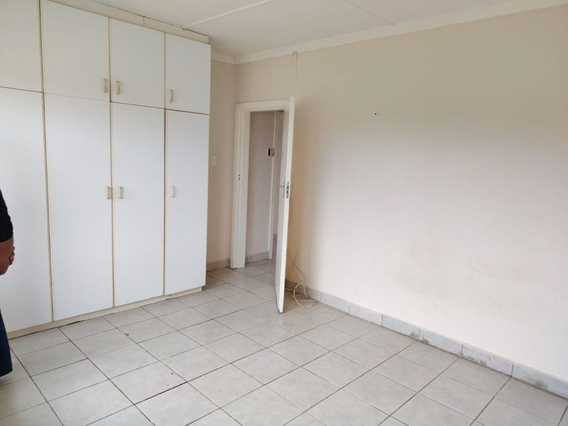 A vacant bedroom featuring white built-in cupboards and neutral tiled flooring, offering a blank canvas for potential interior updates.