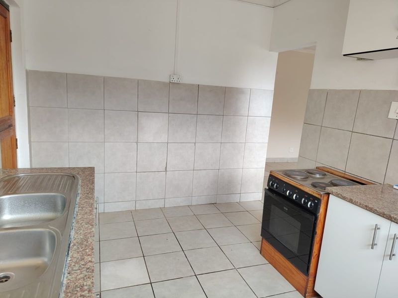 A functional kitchen featuring a double bowl stainless steel sink, granite countertops, tiled splashbacks, and a freestanding electric stove with an extractor fan.