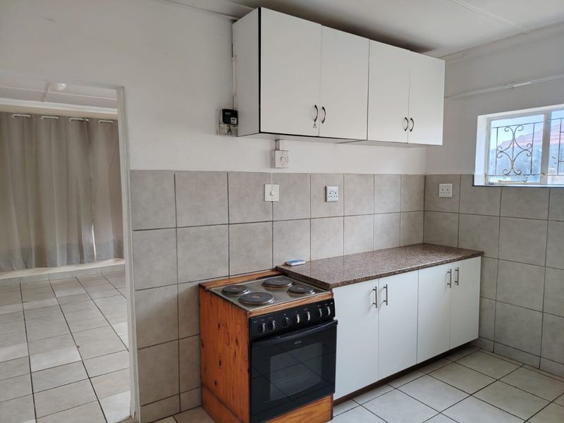 A functional kitchen featuring tiled flooring, a tiled backsplash, built-in cabinetry, and a freestanding electric stove.