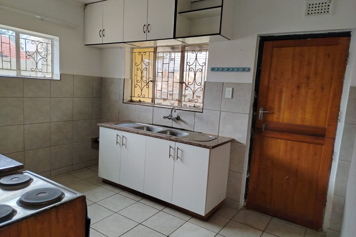 A functional kitchen featuring tiled flooring, a double basin sink, built-in cabinetry, and an electric stove, with security bars on the windows.
