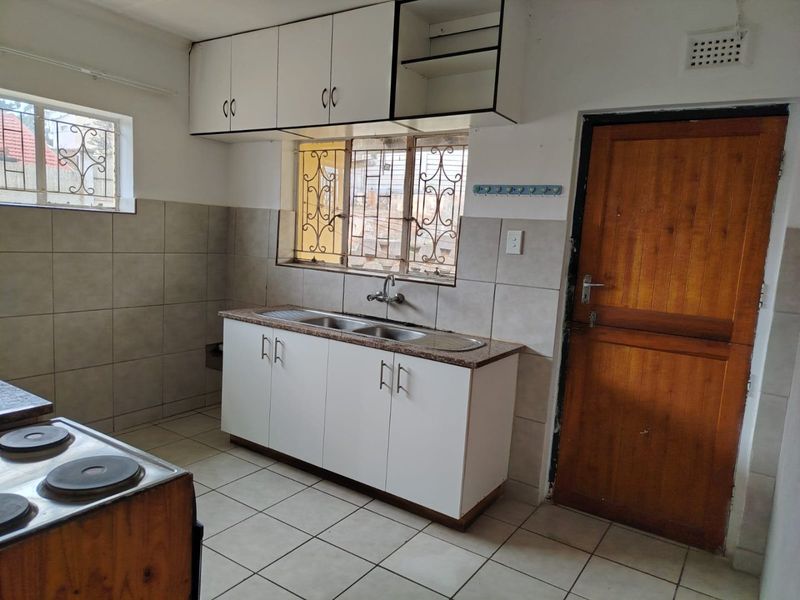 A functional kitchen featuring tiled flooring, a double basin sink, built-in cabinetry, and an electric stove, with security bars on the windows.