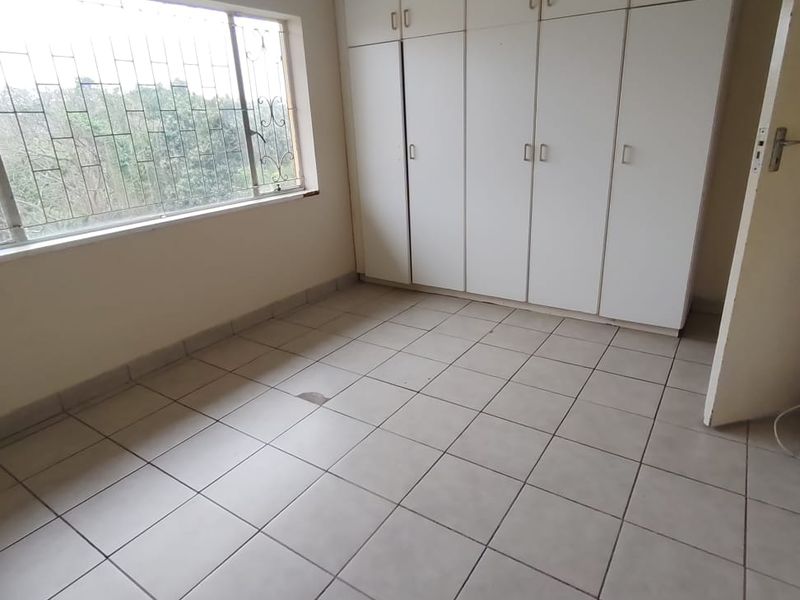 An empty bedroom featuring tiled flooring, built-in white cupboards, and a window fitted with security bars.
