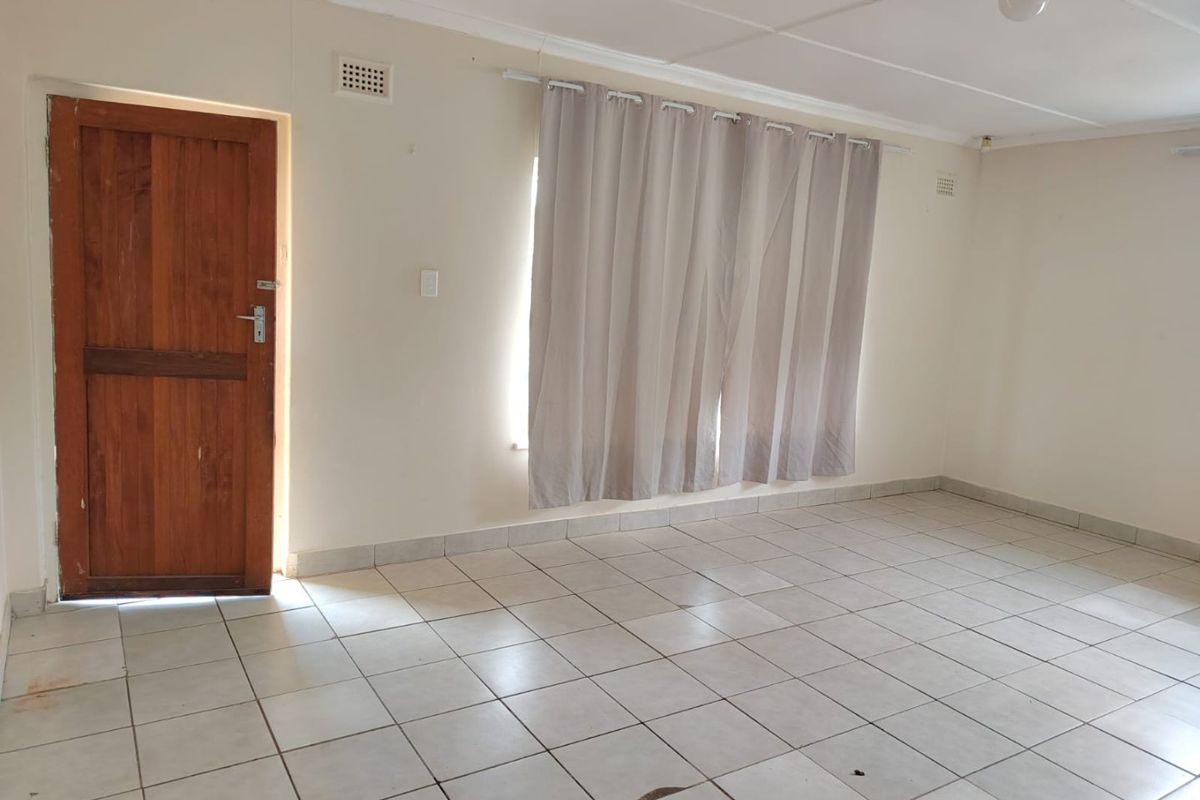 An empty living room featuring neutral tiled flooring, a solid wooden door, and simple ceiling lighting, offering a blank canvas for interior design.