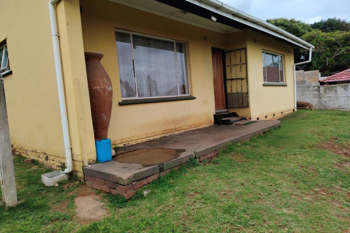 Rear exterior view of the house featuring a concrete patio, brick foundation, and metal window frames, showing signs of wear and exterior wall staining.