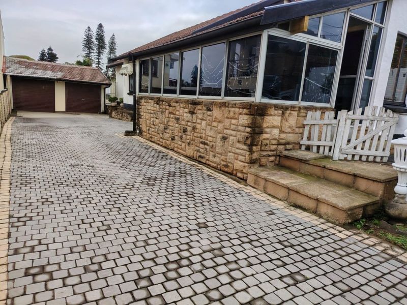 Exterior view of the property featuring a paved driveway, stone-clad facade, and a detached garage with a tiled roof.