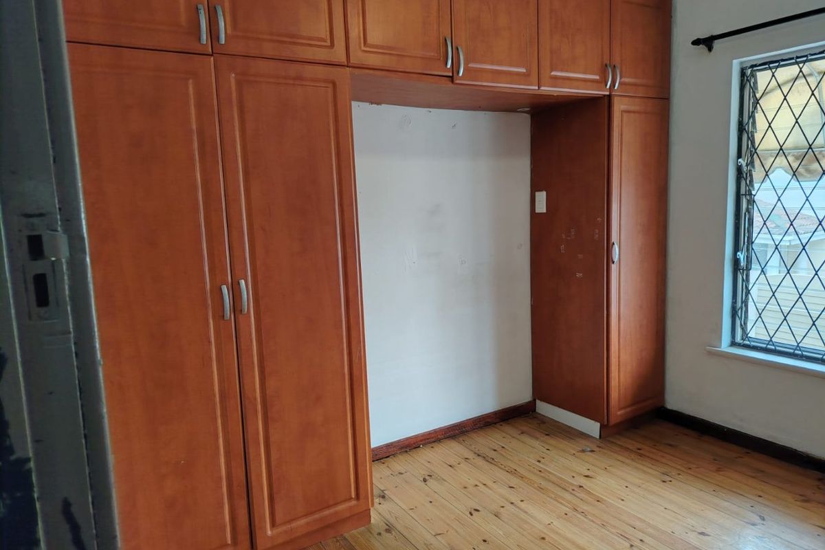 A bedroom featuring built-in wooden cupboards, polished wooden flooring, and a diamond-patterned window, offering a functional space ready for personalization.