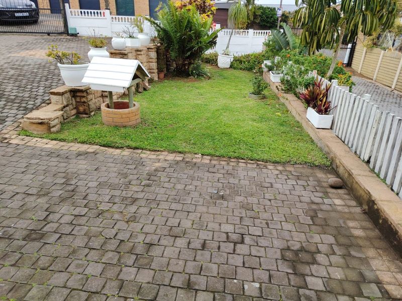 A landscaped front garden area featuring a paved driveway, stone retaining walls, a decorative wishing well, and white picket fencing.