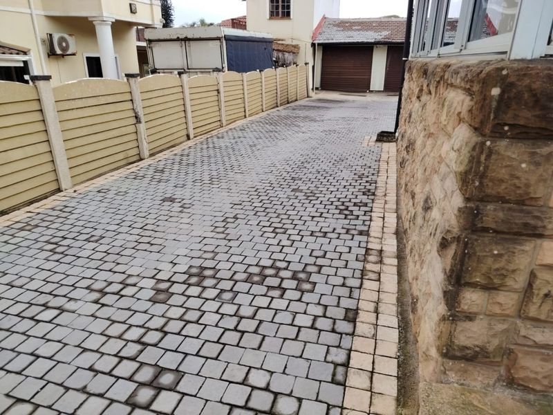 A paved driveway leading to garage doors, featuring stone cladding on the side wall and a precast concrete boundary fence.