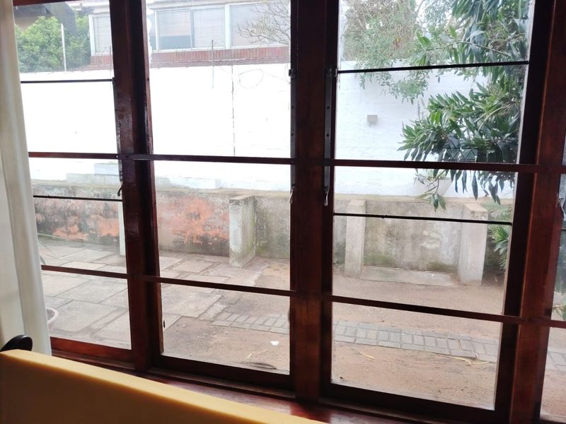 View through timber-framed windows looking out onto a paved patio area with a weathered retaining wall and exterior boundary wall.