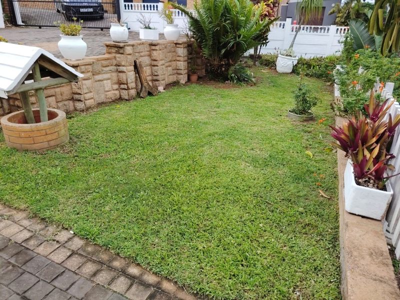 A well-maintained residential garden featuring a green lawn, stone retaining wall, and a decorative brick wishing well feature.