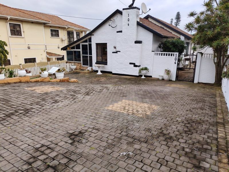 Front exterior view of a house featuring a paved driveway, a prominent chimney, and a secure gated entrance.
