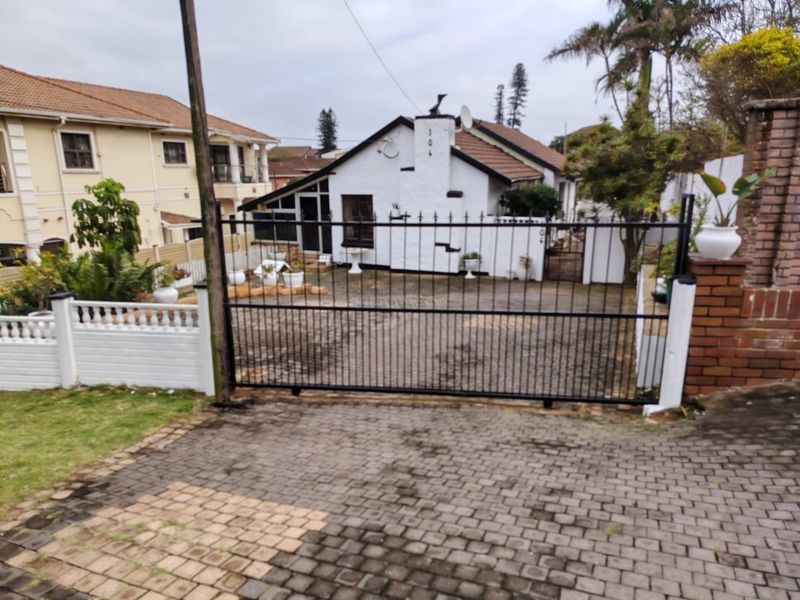Front view of the property featuring a paved driveway, secure metal gate, and a white-painted exterior facade with a tiled roof.