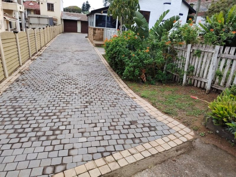 A paved driveway leading to a double garage, bordered by a precast concrete wall and a wooden picket fence with established garden beds.