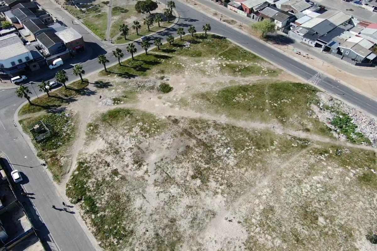 Aerial view of a vacant residential plot situated at a street corner, featuring surrounding paved roads and established palm trees.
