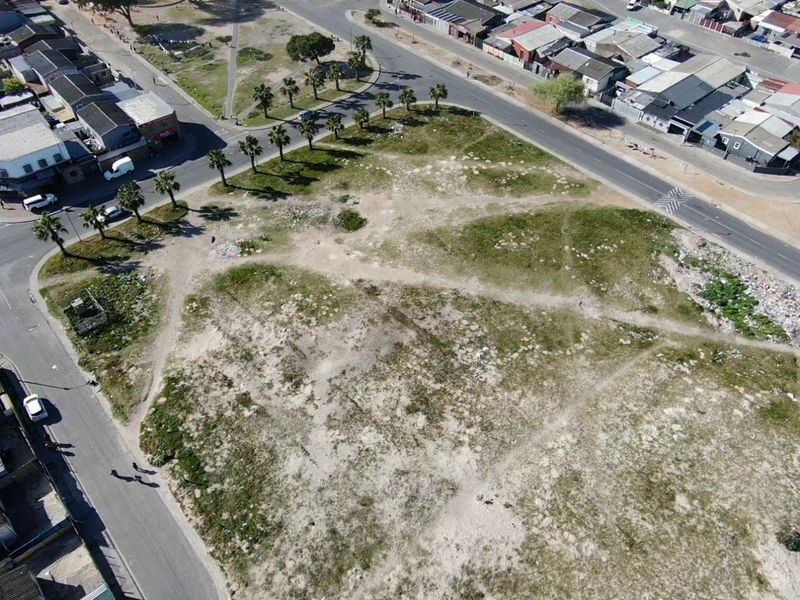 Aerial view of a vacant residential plot situated at a street corner, featuring surrounding paved roads and established palm trees.